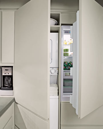 In the kitchen, one wall houses a refrigerator and washer and dryer behind cabinet doors, as well as a toaster and coffeemaker in an appliance In the kitchen, one wall houses a refrigerator and washer and dryer behind cabinet doors, as well as a toaster and coffeemaker in an appliance