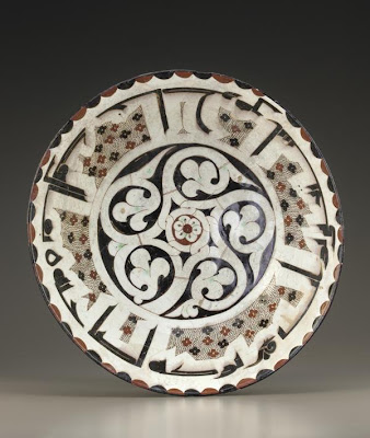 Bowl | Origin:  Iran | Period: 10th century  Samanid period | Details:  This deep bowl exemplifies the high technical quality and compositional sophistication achieved in 10th-century ceramics from northeastern Iran. Its central decoration consists of an abstract tree with five branches ending in palmettes and revolving around a small rosette. The dominant counter-clockwise movement of the stems is subtlely reversed by a branch to the trunk's leftÂ— a shift that ingeniously draws attention to the ovoid mark at the beginning of the Arabic inscription below. This inscription is bordered at the rim by a band of red and black scallops and on the walls by a series of irregular panels following the contours of the letters. It translates as follows: "It is said that he is content with his own opinion runs into danger. Blessing to the owner." | Type: Earthenware painted under glaze | Size: H: 11.2  W: 39.3   D: 39.3  cm | Museum Code: F1957.24 | Photograph and description taken from Freer and the Sackler (Smithsonian) Museums.