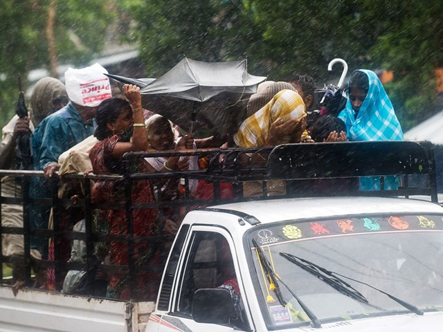 Villagers try to cover themselves from heavy rainfall and strong winds as they ride a pickup in Srikakulam district on Saturday, 12 OCtober 2013. India evacuated over 600,000 people as the massive cyclone Phailin closed in. Photo: Manan Vatsyayana / AFP / Getty Images