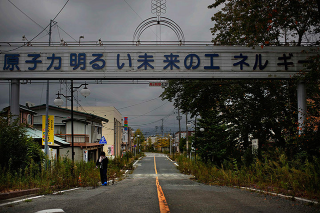 A woman paying a brief visit to her home walks under a sign reading 'Nuclear power – the energy for a better future', at the entrance of the empty Futaba town. Decades ago the citizens ofFutaba took such pride in hosting part of the Fukushima Daiichi nuclear complex that they built a sign over a promenade proclaiming that atomic power made their town prosperous. Photo: Damir Sagolj / Reuters