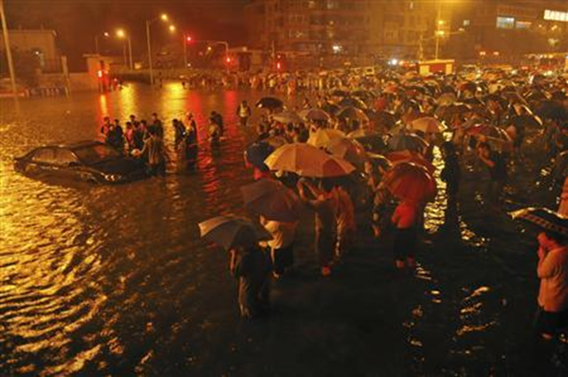 Rescuers and residents stand next to a stranded car which is being pulled up from a flooded street under the Guangqumen overpass amid heavy rainfall in Beijing, 21 July 2012. According to local media, a driver of another submerged car was confirmed dead in hospital after being pulled out critically injured at this street. The heaviest rains in 61 years that lashed Beijing Saturday have left at least 37 people dead, cutting off traffic and also severely disrupted air traffic. REUTERS / Stringer