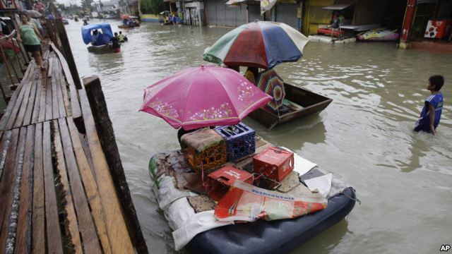 Residents use makeshift floats as others cross a makeshift bridge built over a flooded road in suburban Pasig, east of Manila, Philippines, 15 August 2012. AP