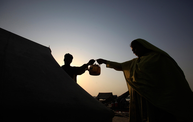 A female refugee passes a kettle of tea to her husband in preparation to break their fast during the holy month of Ramadan at a camp for flood victims in Nowshera, northwest Pakistan on 2 August 2011. The couple were forced from their home by floods last year that killed about 2,000 people and left 11 million homeless. Fayaz Aziz / Reuters