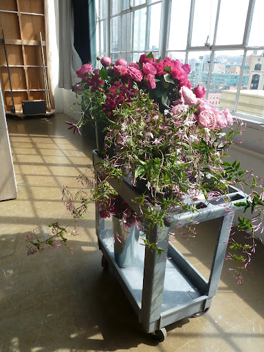A cart holds roses, clematis, and jasmine. We moved it to the sun so the flowers would open up.