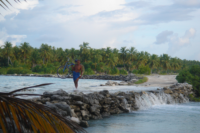 A local villager in Beru, Kiribati crosses a causeway carrying his bike at high tide with the water lapping at his feet, 6 November 2006. Only a few years earlier, this sight was highly uncommon but is now experienced on a regular basis. Photo: Jeremy Mather / flickr