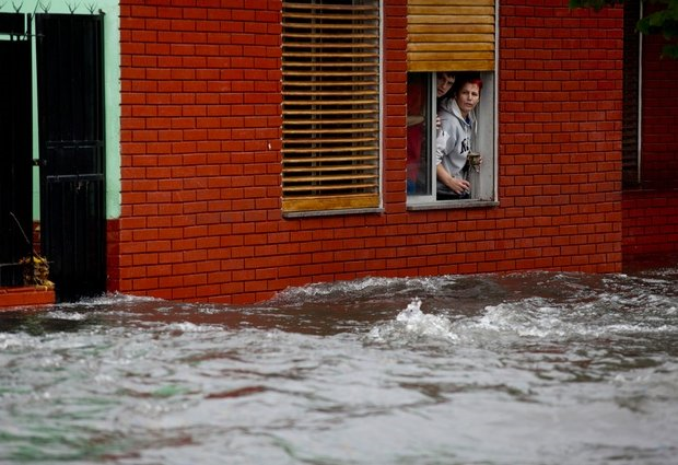 A couple looks at their flooded street from behind their home's window in La Plata, in Argentina's Buenos Aires province, Wednesday, 3 April 2013. At least 35 people were killed by flooding overnight in Argentina's Buenos Aires province, the governor said Wednesday, bringing the overall death toll from days of torrential rains to at least 57 and leaving large stretches of the provincial capital under water. Photo: AP