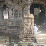 Now we will start our tour of the temple, from west to north, circumanulating the external structure. The guardian image is perhaps portraying Shiva only. Shown here with four hands, carrying damaru, sword, bowl and ram-head. Above the head is shown a snake hood whose tail is shown forming a garland around Shiva's body, and various attendants are standing on either side. Is this the representation of Shiva as a hunter?