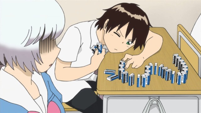 Seki leans down close to his desk as he carefully sets up a domino line using erasers as Rumi watches in shocked disbelief