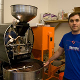 Matt McQuilkin stands next to BCRC's roaster. Behind him is a destoner, which removes debris from coffee after it has been roasting and before it is bagged.