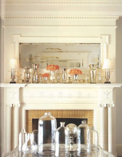On the shelf of a mirrored mantelpiece, reflective mercury-glass lamps, vases, and other vessels provide a warm, luminous setting for the roses that bring the only touch of intense color. On the shelf of a mirrored mantelpiece, reflective mercury-glass lamps, vases, and other vessels provide a warm, luminous setting for the roses that bring the only touch of intense color.
