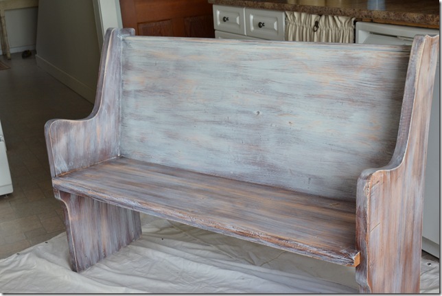 Wood church pew with thin coat of white paint and dark wood grain showing through