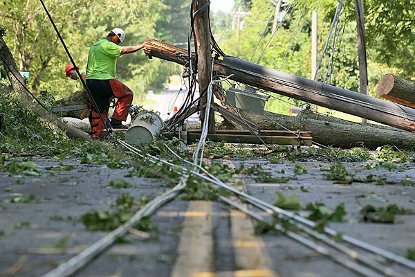 Workers remove debris from fallen tree limbs and a downed utility pole so that power lines can be repaired in Huntington, Md. Scores of homes across the Washington area lost power after a severe thunderstorm, 30 June 2012. Mark Wilson / Getty Images