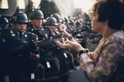 c0 A Vietnam War era picture of a woman putting a flower in the muzzle of a gun.
