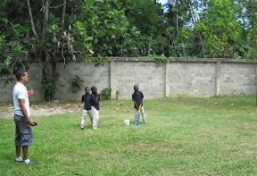 Plaquita.  Memo has the ball ready to throw, Bienvenido is standing with his bat on base, and Miguel Angel is coaching.