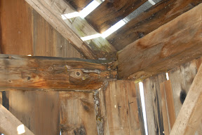 Water damage at the plate, tie, post and rafter is illuminated by light shining through the missing roofing.