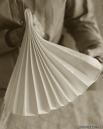 A napkin in an accordion fold, also known as a stemware fold, is an artful accent to the holiday table. Fold the pleats in half as shown, insert the bottom into a glass, and then fan out the top pleats.