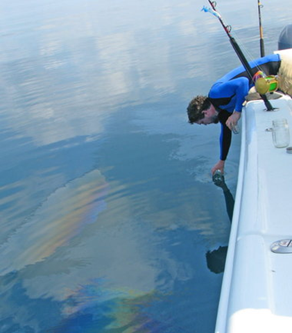The Press-Register's Ben Raines scoops oil where it bubbled to the surface of the Gulf of Mexico on 23 August 2011 within one mile northeast of BP's Macondo well site. Jeff Dute / Press-Register