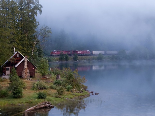 Train pass through a foggy lakefront morning, surrounded by green at Three Valley in Revelstoke, British Columbia, Canada 