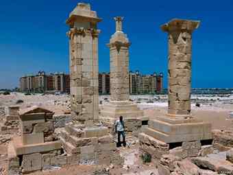 With a five star hotel in the background, a man walks by restored Roman pillar tombs of the ancient city of Leukaspis.
