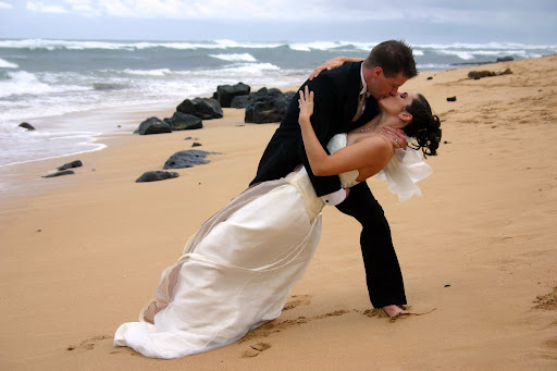 A bride and groom share a kiss on the beachwearing bridal gown