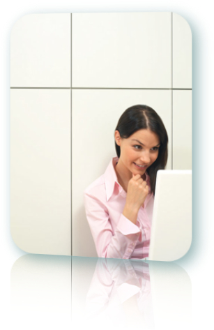 Smiling woman wearing a pink shirt and sitting in a white room looking at a computer screen.