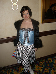 A young woman wearing a flapper-style dress with an applique'd bow tie and an off-the-shoulder fuzzy coat, much like the Second Doctor.