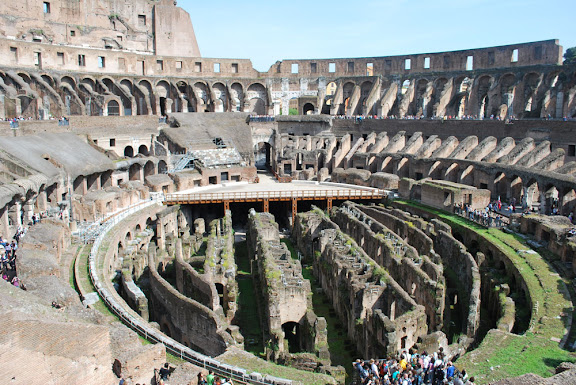 a large circular structure with many arches with Colosseum in the background