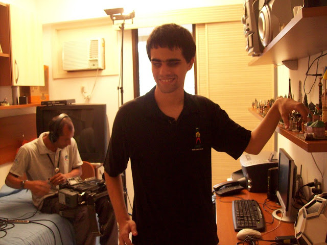 Legenda da Foto :Em destaque, Marcos mostra uma de suas miniaturas. Ao fundo, vê-se o camaraman da Record preparando o equipamento