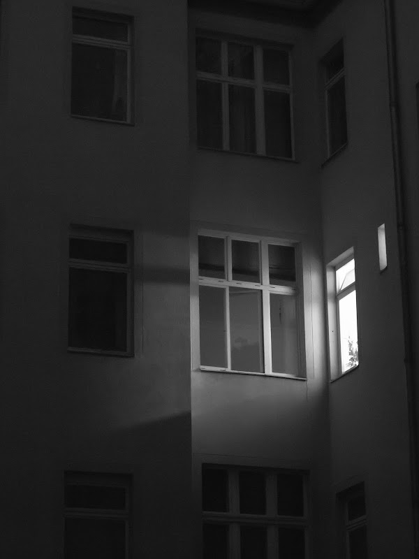 [FASSADE IN SCHWARZWEISS UM 2 UHR MORGENS. AUF DER RECHTEN SEITE IST EIN FENSTER ERLEUCHTET. DIE ANDEREN FENSTER DER FASSADE SIND DUNKEL]