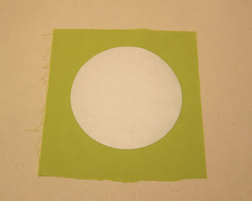 Iron one freezer paper circle onto the wrong side of a piece of fabric, shiny side down.