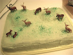 Plastic deer frolicking through the icing of a sheet cake.