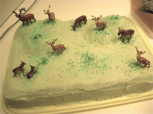 Plastic deer frolicking through the icing of a sheet cake.