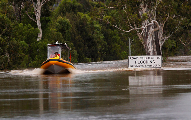 An emergency personnel boat motors past a street sign partially covered by floodwaters 6km south of Rockhampton on January 3, 2011. The sign reads, 'Road subject to flooding. Indicators show depth.' No indicators are visible. REUTERS / Daniel Munoz