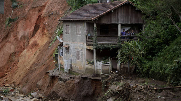 Residents stand on the porch of their home at the edge of landslide damage in the Caleme neighbourhood of Teresopolis, Brazil, 14 January 2011. Felipe Dana / AP
