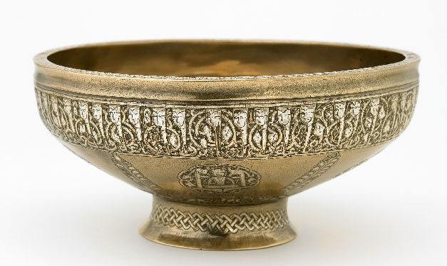 With the growing sophistication of inlay techniques in the thirteenth century, the art of calligraphy began to play a central role on metal objects. As this elegant stem bowl indicates, inscriptions often functioned as the principal means of embellishment. Most inscriptions consisted of blessings and short prayers addressed to anonymous patrons. The inscription on this bowl is particularly notable for its human-headed letters, a highly inventive style that developed in the thirteenth century and was used exclusively on metalwork intended for use in secular settings. Present-day Afghanistan, Herat. Early 13th century. 8.7 x 19.5 x 19.5 cm. Kufic script. Courtesy of the Freer Gallery of Art, Smithsonian Institution.