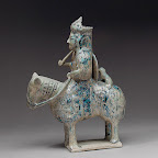 This figurine represents the relatively rare sculptural tradition within Islamic art. Although the function of this and other such Seljuq equestrian figures is not entirely known, they appear to portray significant personages. Here the overall symbolism conveyed is that of a warrior or hunter: the rider holds a cup, carries a short staff, and bears what appears to be a shield. The small animal seated behind the rider may be a hunting cheetah, and the hollowness of the object's upper section suggests a container-like function.