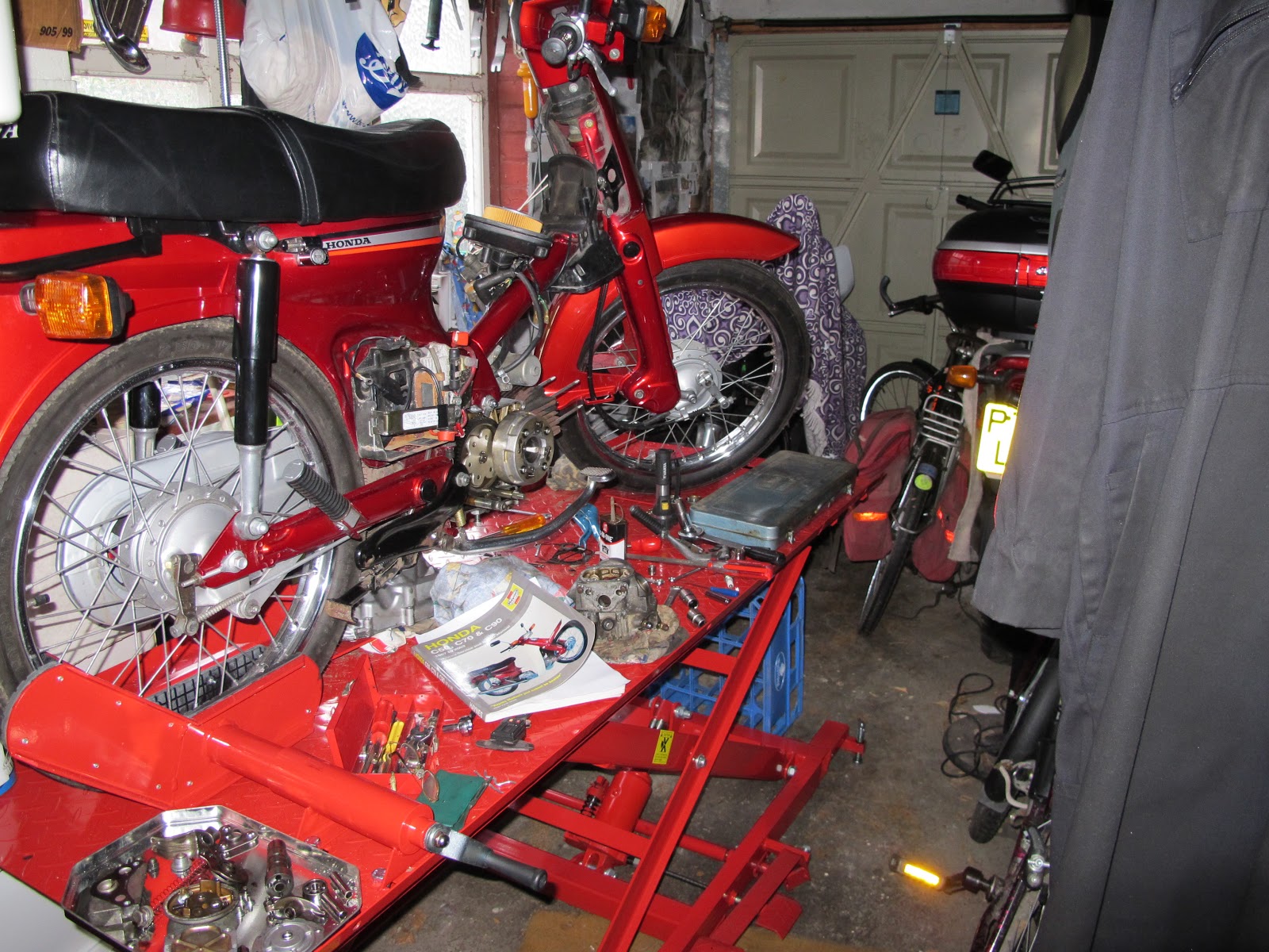 A general view of the C90 on the bike lift, removed parts, tools, and the  Haynes manual