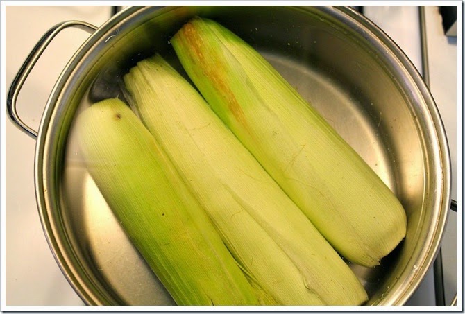 adding corn with husks in a large pot of water 
