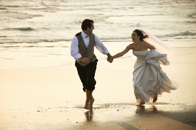 Caucasian prime adult male groom and female bride running barefoot on beach.