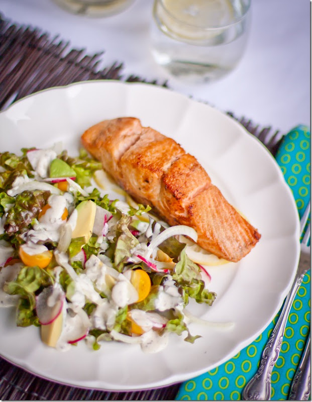 Top view of fresh salad with homemade buttermilk dressing with buttered salmon on a white decorative plate.
