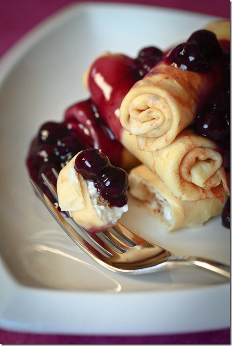 Easy Farmer’s cheese filled crepes topped with a blueberry sauce with a fork. 