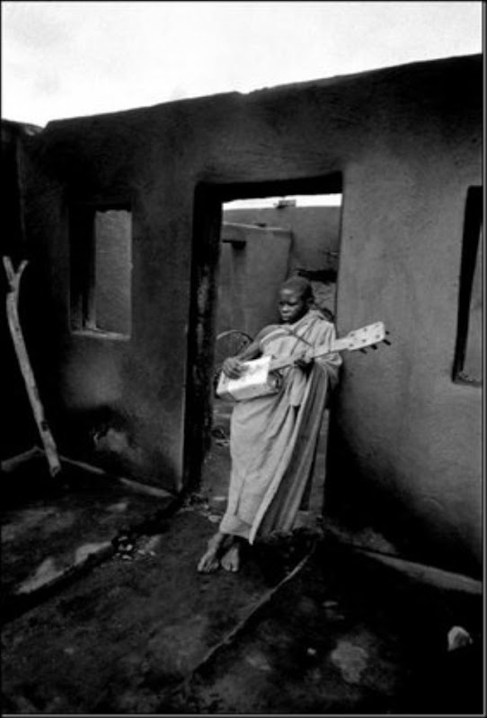 MASERU, Lesotho — A boy plays a guitar made from an oil can in the burned out ruins of his home during political violence, 1961.