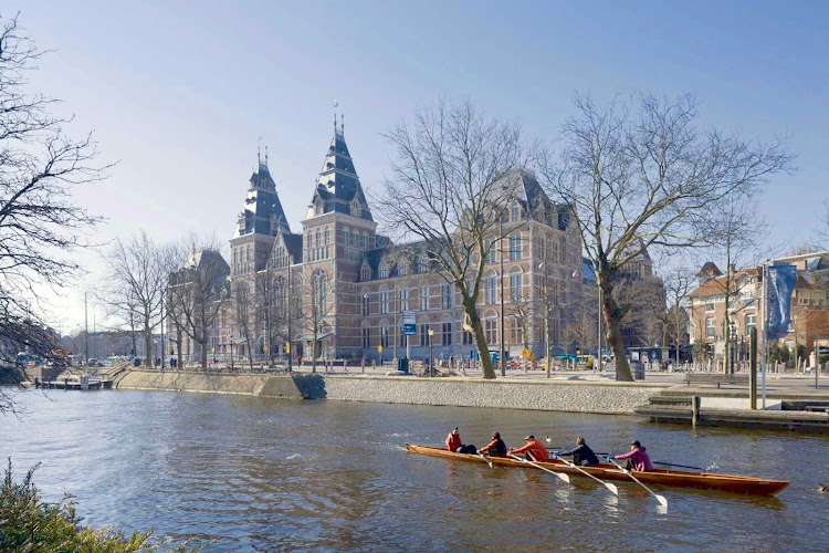 Oarsmen glide past the Rijksmuseum in Amsterdam, Netherlands.