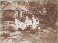 Een gedekte tafel in de tropen met daaraan mensen gekleed in het wit.