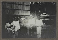 Vier Indische mannen en vrouwen staand voor een houten trap bij een huis