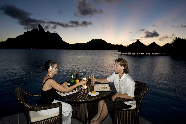 Enjoy a sunset dinner at the St. Regis Bora Bora Resort during your cruise vacation.
