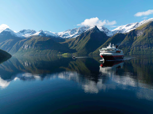 Hurtigruten's Nordnorge sailing during an autumn day along the Hjørundfjorden fjord in Norway where the water has the appearance of glass.