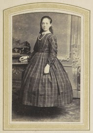 Portret van een meisje in een geruite jurk bij een tafel met boeken