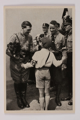 Cigarette card with an image of a smiling Hitler holding roses and greeting a Hitler Youth member 2012.68.8 front