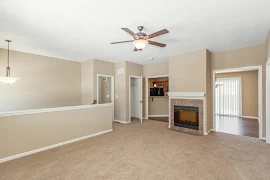 Living area with tan walls, tan carpet, a fireplace with tan tile, ceiling fan, and access to the dining area and kitchen